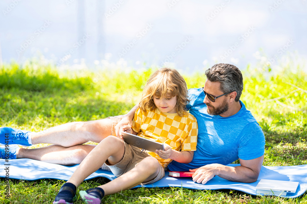 Fototapeta premium childhood school education. son with father bonding in summer. family education of father and son kid. Father shapes son education. Father and son relax in park. Parent reading with child