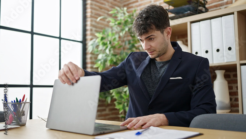 Young hispanic man business worker opening laptop at office