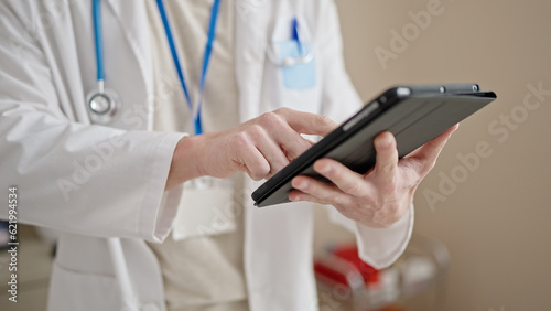 Young hispanic man doctor using touchpad at clinic