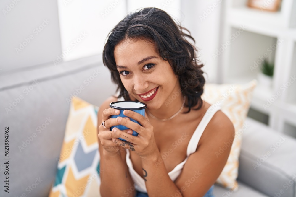 Young beautiful hispanic woman drinking coffee sitting on sofa at home Young beautiful hispanic woman drinking coffee sitting on sofa at home
