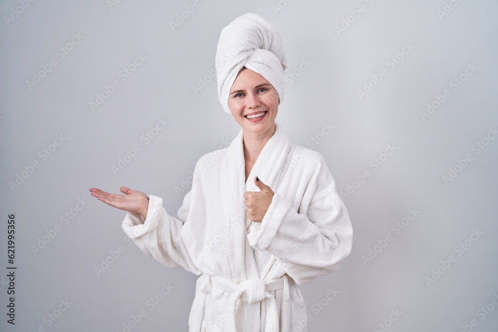 Blonde caucasian woman wearing bathrobe showing palm hand and doing ok gesture with thumbs up, smiling happy and cheerful Blonde caucasian woman wearing bathrobe showing palm hand and doing ok gesture with thumbs up, smiling happy and cheerful