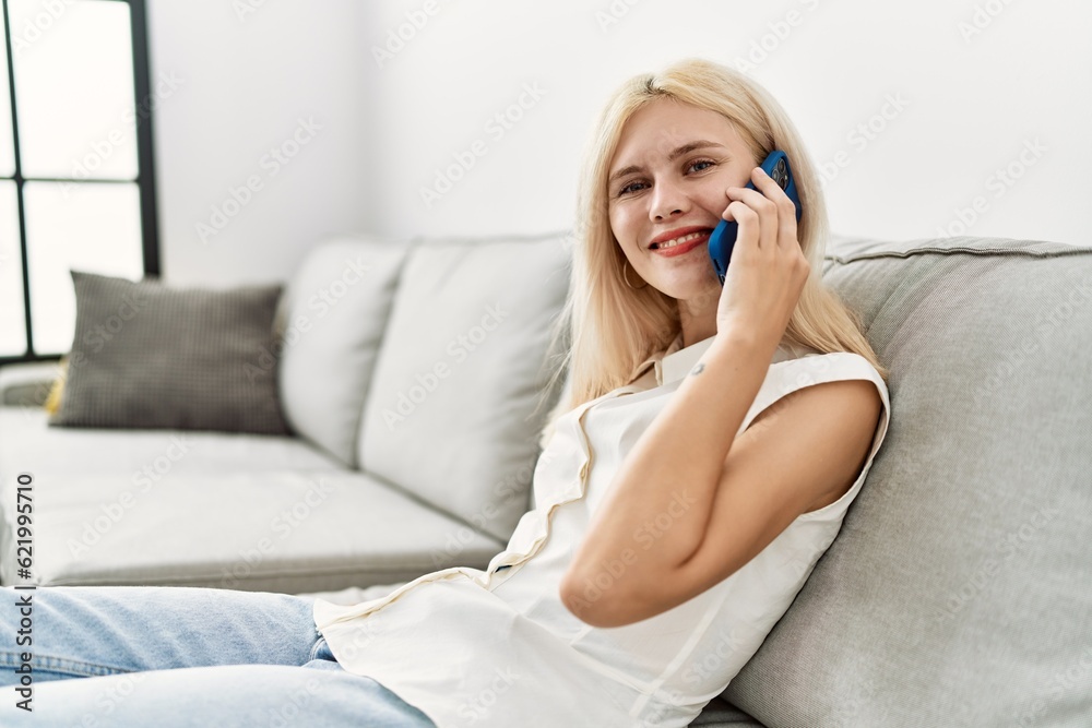 Young blonde woman speaking on the phone sitting on sofa at home Young blonde woman speaking on the phone sitting on sofa at home