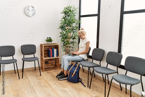 Young blonde woman using laptop sitting on chair at waiting room