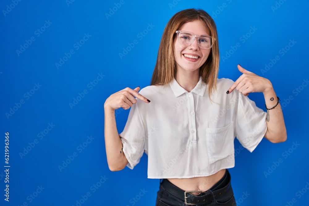 Fototapeta premium Beautiful woman standing over blue background looking confident with smile on face, pointing oneself with fingers proud and happy.
