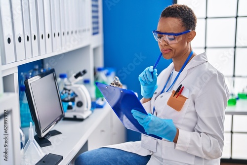 African american woman scientist writing on document with doubt expression at laboratory