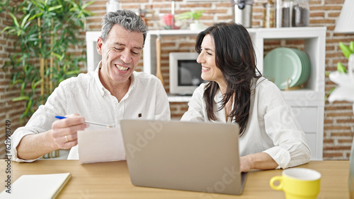 Senior man and woman couple using laptop reading document at dinning room