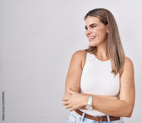 Hispanic young woman standing over white background looking away to side with smile on face, natural expression. laughing confident.