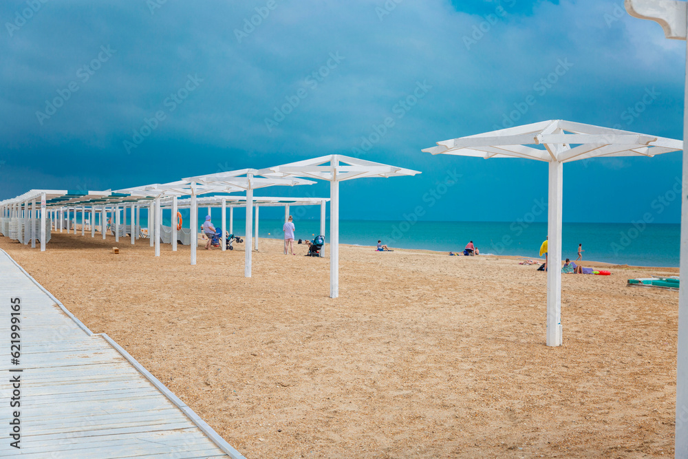 White wooden poles on the sandy beach for umbrellas and awnings. Bathing and resting people on a sunny day. White wooden poles on the sandy beach for umbrellas and awnings. Bathing and resting people on a sunny day.