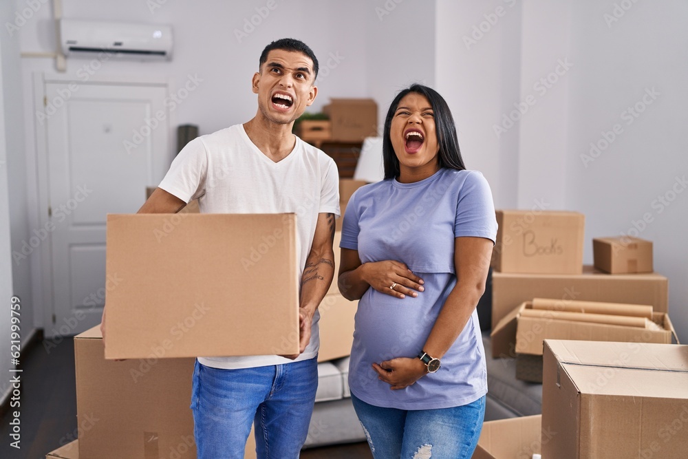 Young hispanic couple expecting a baby moving to a new home angry and mad screaming frustrated and furious, shouting with anger looking up. Young hispanic couple expecting a baby moving to a new home angry and mad screaming frustrated and furious, shouting with anger looking up.