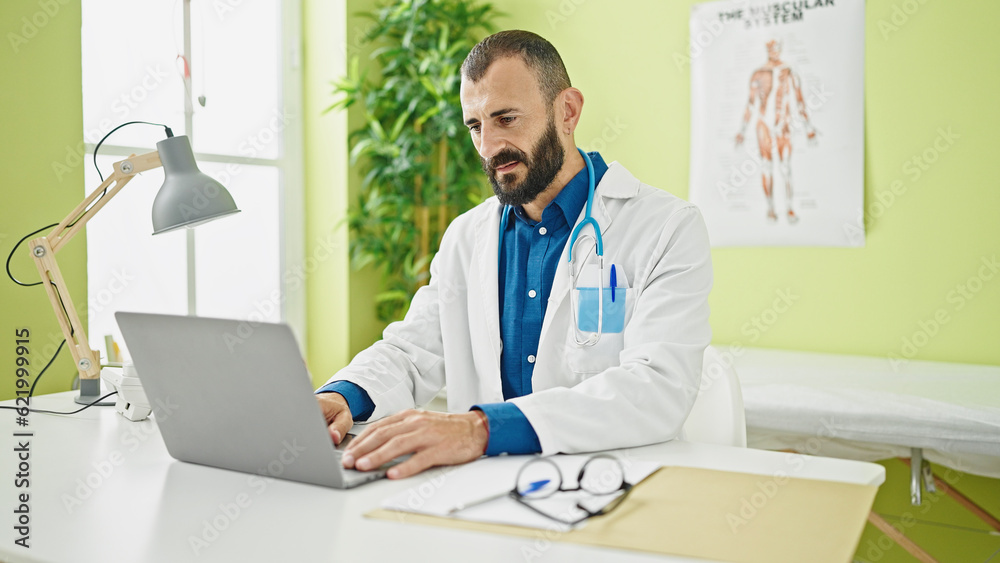 Young hispanic man doctor using laptop working at clinic