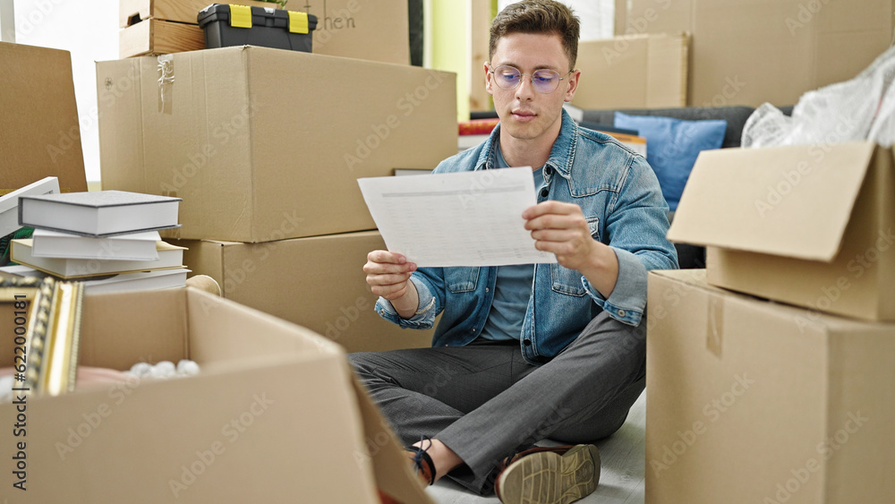 Young hispanic man sitting on floor reading document at new home Young hispanic man sitting on floor reading document at new home
