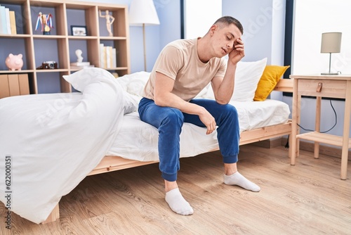 Young hispanic man stressed sitting on bed at bedroom