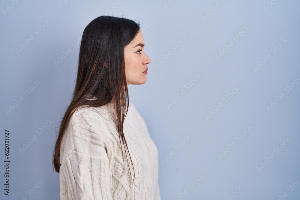 Young brunette woman standing over blue background looking to side, relax profile pose with natural face and confident smile. Young brunette woman standing over blue background looking to side, relax profile pose with natural face and confident smile.
