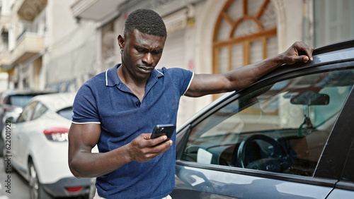 African american man using smartphone leaning on car at street