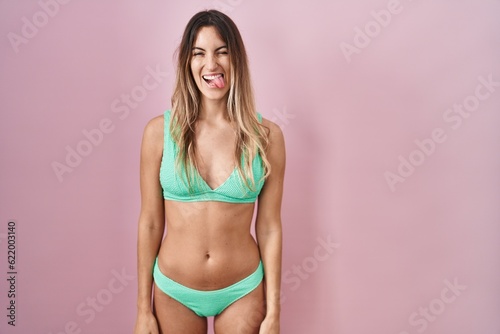Young hispanic woman wearing bikini over pink background sticking tongue out happy with funny expression. emotion concept. © Krakenimages.com