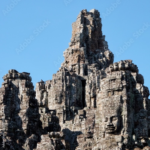 The majestic stone towers of the Bayon Temple in Cambodia, an iconic symbol of Khmer architecture, under a clear blue sky.