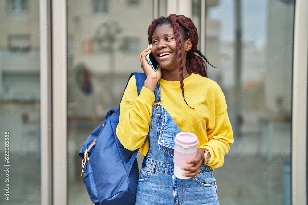 Fototapeta premium African american woman student talking on smartphone drinking coffee at university