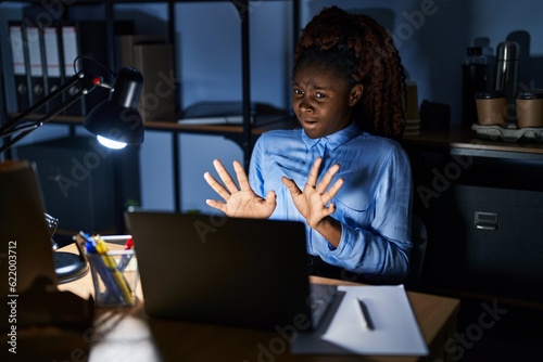 African woman working at the office at night afraid and terrified with fear expression stop gesture with hands, shouting in shock. panic concept.