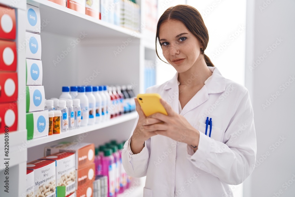 Young woman pharmacist using smartphone working at pharmacy