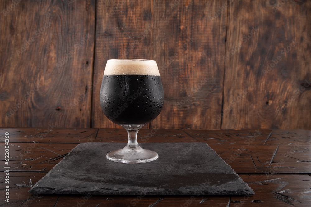 A glass of dark beer on a wood background. Beer on a slate tray. Serving stout beer.