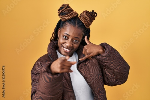 African woman with braided hair standing over yellow background smiling doing talking on the telephone gesture and pointing to you. call me. © Krakenimages.com