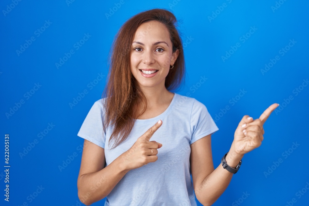 Brunette woman standing over blue background smiling and looking at the camera pointing with two hands and fingers to the side. Brunette woman standing over blue background smiling and looking at the camera pointing with two hands and fingers to the side.