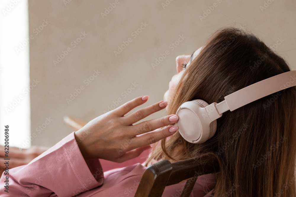 Naklejka premium A young beautiful woman listening to music with headphones with her eyes closed sitting on a retro wooden chair.. Peace, harmony, relaxation and relaxation.