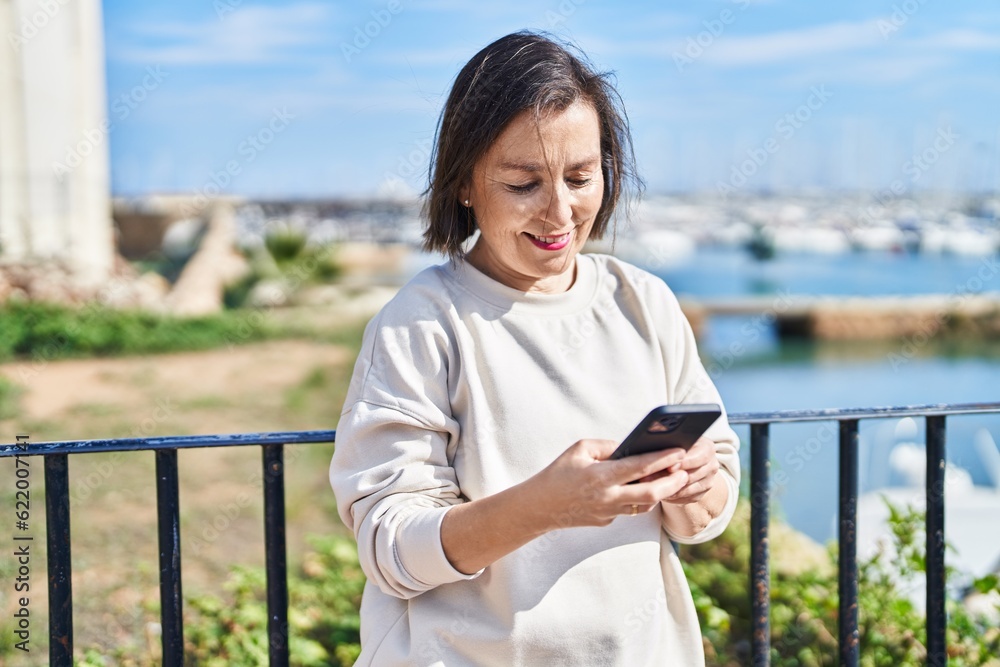 Middle age woman smiling confident using smartphone at seaside