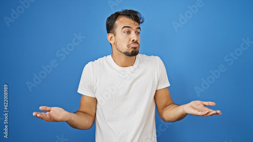 Obraz na płótnie Young hispanic man standing clueless over isolated blue background