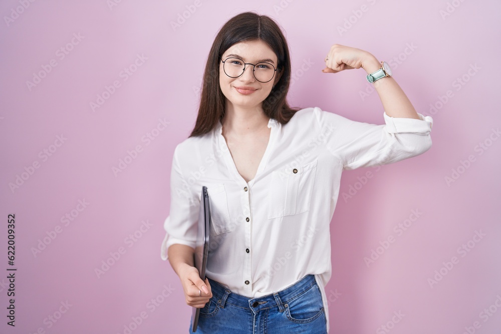 Young caucasian woman holding laptop strong person showing arm muscle, confident and proud of power Young caucasian woman holding laptop strong person showing arm muscle, confident and proud of power