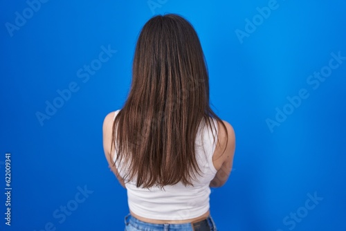 Young caucasian woman standing over blue background standing backwards looking away with crossed arms