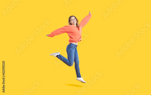 Overjoyed millennial girl isolated on yellow studio background jump dance. Smiling young Caucasian woman have fun make dancer moves enjoy loud music. Entertainment and hobby. © Studio Romantic