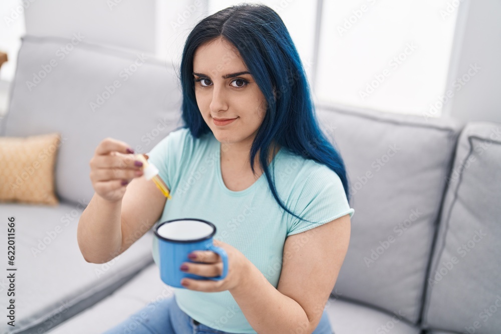 Young caucasian woman pouring liquid on cup sitting on sofa at home Young caucasian woman pouring liquid on cup sitting on sofa at home