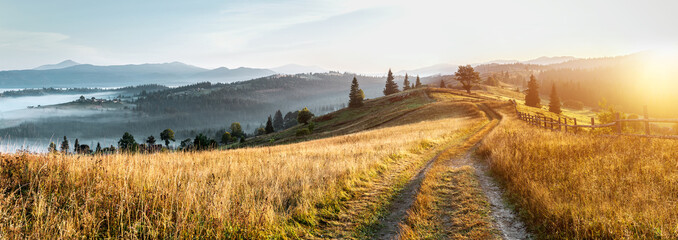 Mountain autumn landscape. Grassy road to the mountains hills during sunset. Nature background