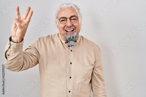 Middle age man with grey hair standing over isolated background showing and pointing up with fingers number three while smiling confident and happy.