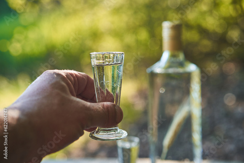Cheers, shot of polish vodka in vintage glass in dirty worker hand after hard shift in the factory as a dangerous refresment or mark of addiction. Picture is taken outside, during sunny summer sunset.