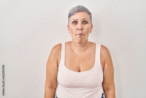 Middle age caucasian woman standing over white background making fish face with lips, crazy and comical gesture. funny expression.