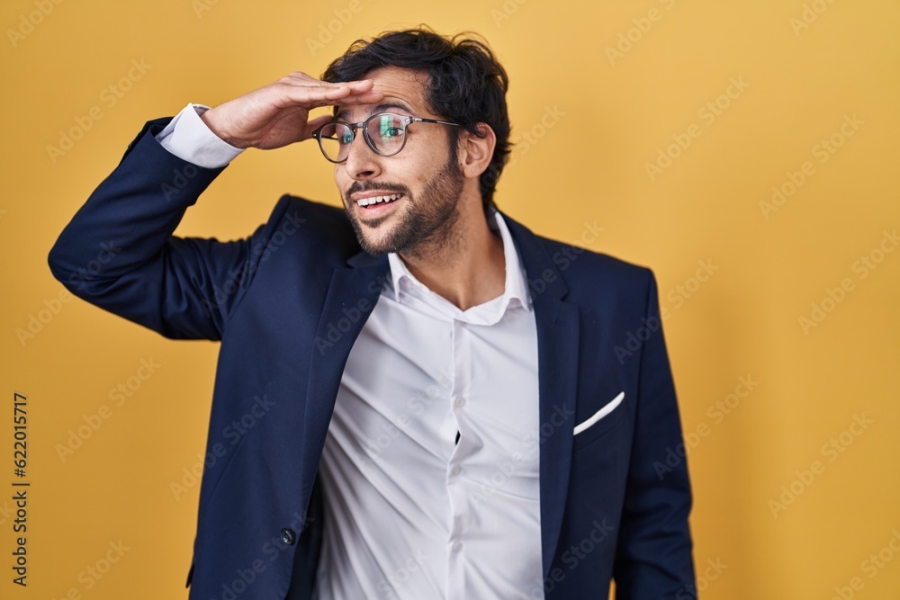 Handsome latin man standing over yellow background very happy and smiling looking far away with hand over head. searching concept. Handsome latin man standing over yellow background very happy and smiling looking far away with hand over head. searching concept.