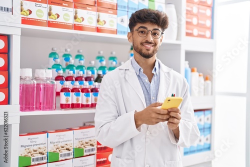 Young arab man pharmacist using smartphone standing at pharmacy