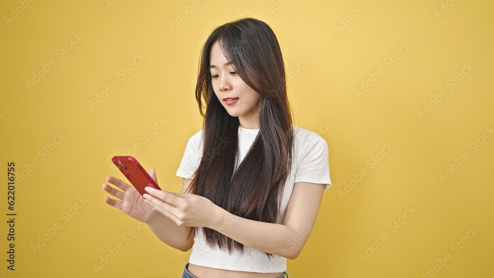 Young chinese woman using smartphone with relaxed expression over isolated yellow background Young chinese woman using smartphone with relaxed expression over isolated yellow background