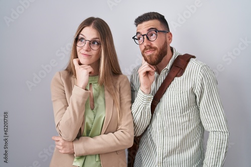 Young couple standing over white background with hand on chin thinking about question, pensive expression. smiling with thoughtful face. doubt concept.
