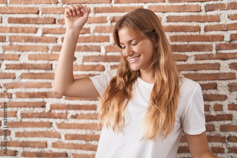 Young caucasian woman standing over bricks wall dancing happy and cheerful, smiling moving casual and confident listening to music Young caucasian woman standing over bricks wall dancing happy and cheerful, smiling moving casual and confident listening to music