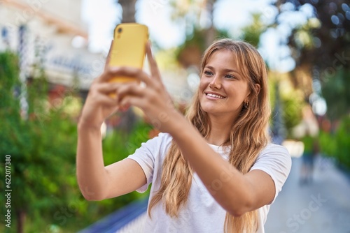 Young blonde girl smiling confident making selfie by the smartphone at park