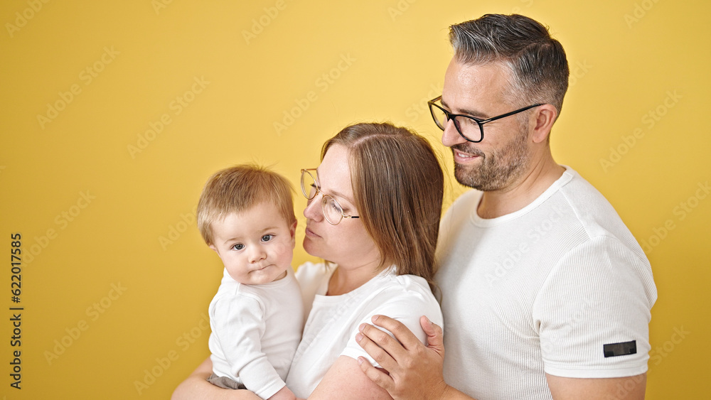 Family of mother, father and baby smiling together over isolated yellow background