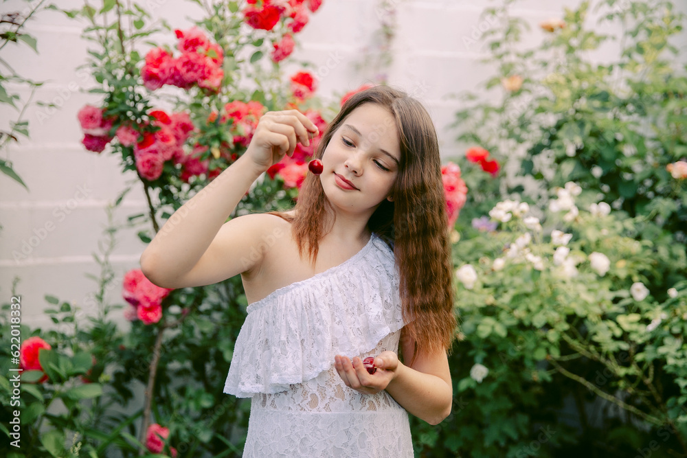 Beautiful teenage girl in a white dress picking cherries or cherries, looks at her Beautiful teenage girl in a white dress picking cherries or cherries, looks at her