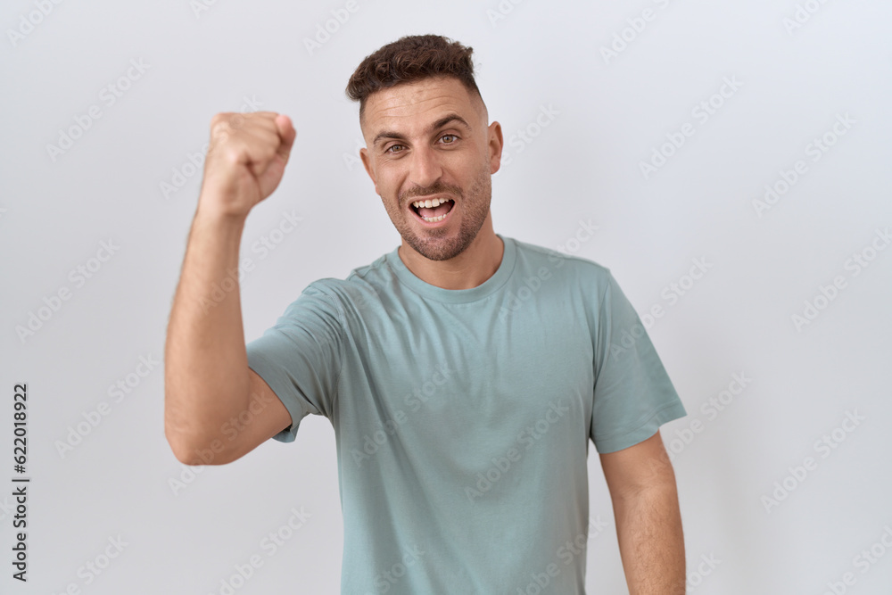 Hispanic man with beard standing over white background angry and mad raising fist frustrated and furious while shouting with anger. rage and aggressive concept. Hispanic man with beard standing over white background angry and mad raising fist frustrated and furious while shouting with anger. rage and aggressive concept.