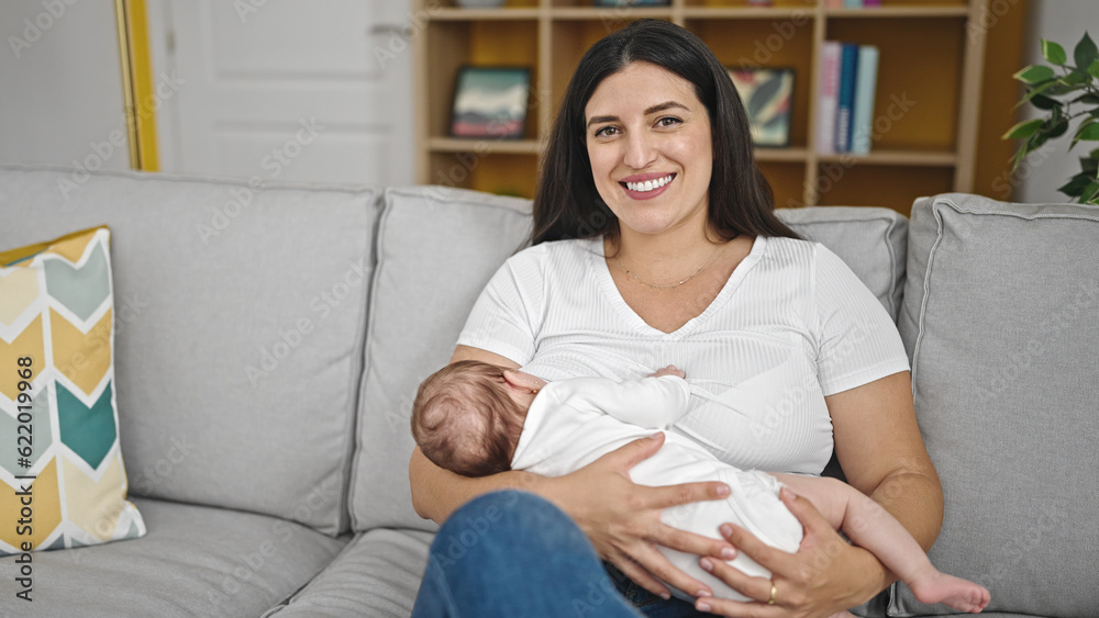 Mother and baby daughter sitting on sofa breastfeeding at home Mother and baby daughter sitting on sofa breastfeeding at home