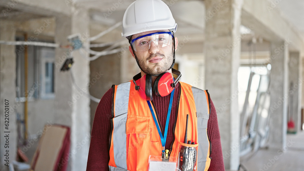 Young hispanic man builder standing with serious face at construction site Young hispanic man builder standing with serious face at construction site