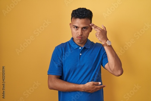 Foto Young hispanic man standing over yellow background shooting and killing oneself pointing hand and fingers to head like gun, suicide gesture