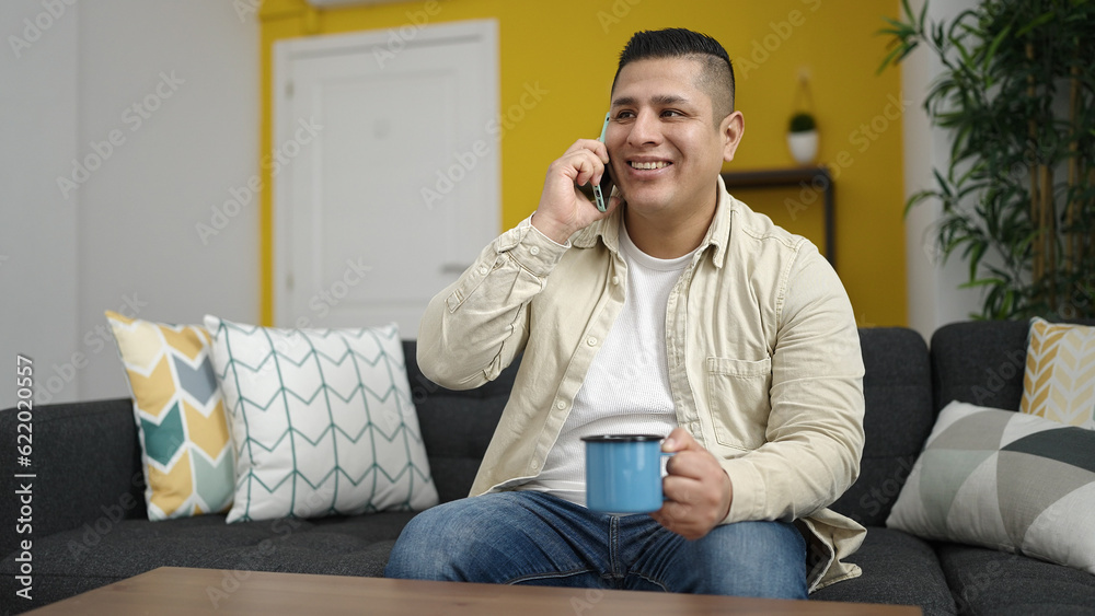 Young hispanic man speaking on the phone drinking a cup of coffee at home Young hispanic man speaking on the phone drinking a cup of coffee at home